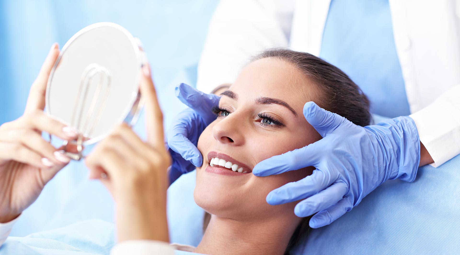 Woman receiving facial treatment with blue gloves and mirror held up by a professional.
