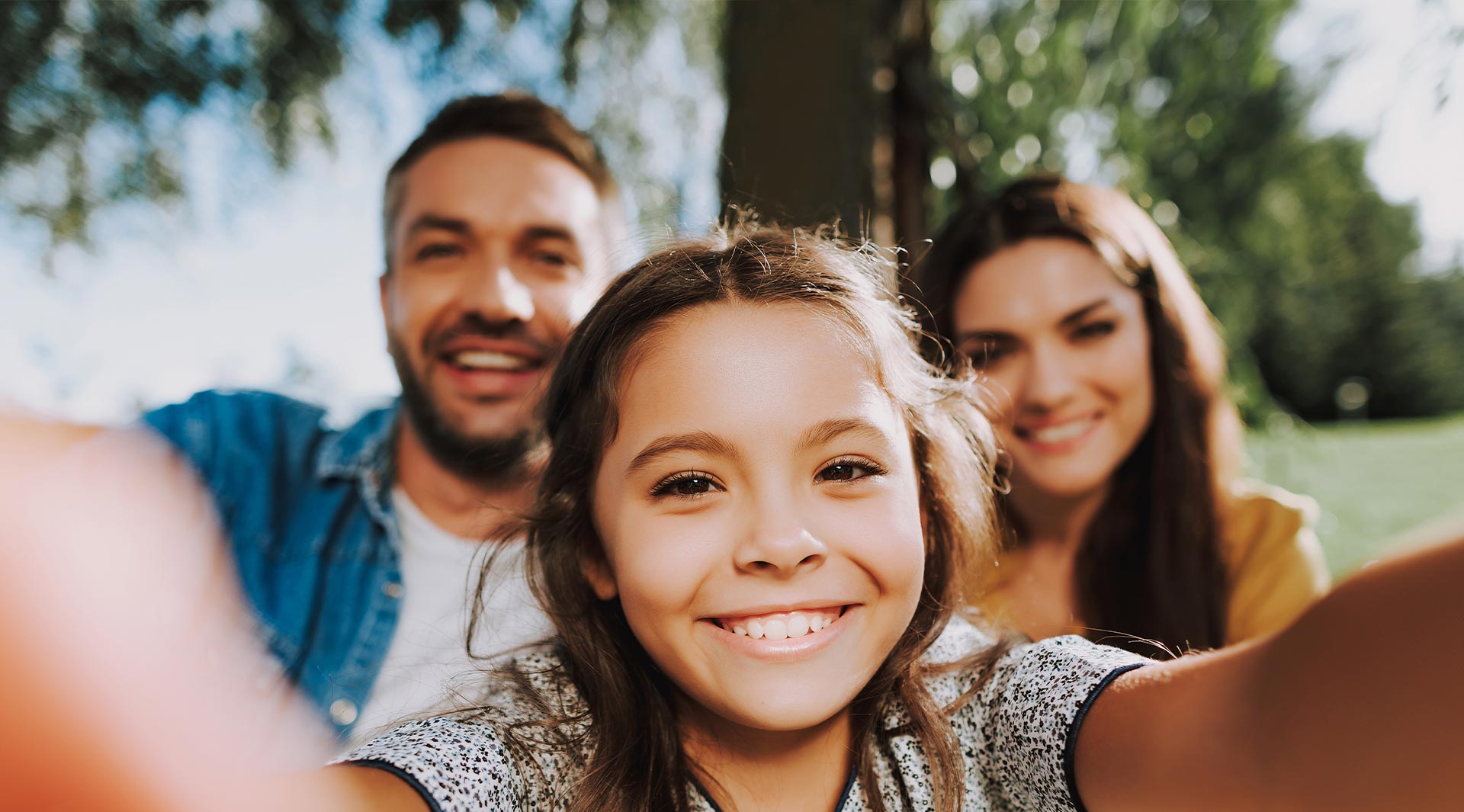 A family with a child taking a selfie together outdoors during the day.