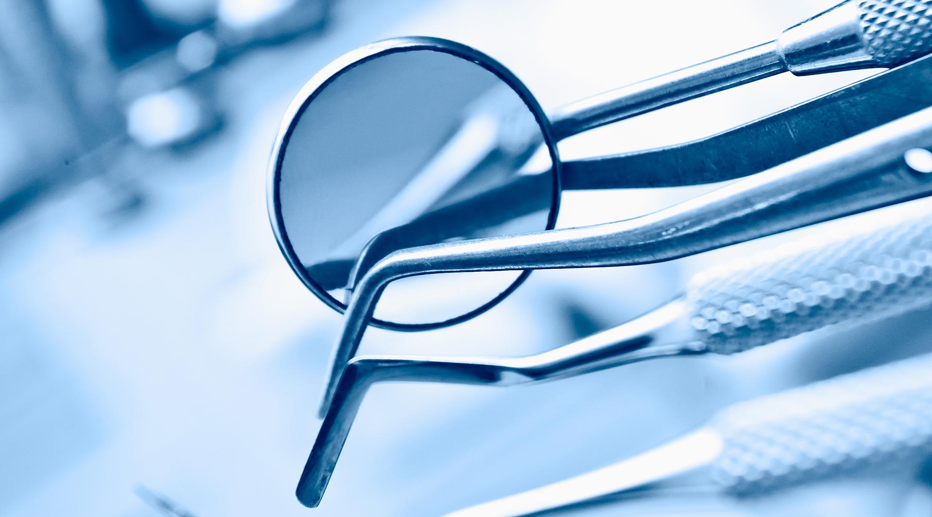 The image depicts a pair of eyeglasses with an eyelet resting on top of a collection of surgical instruments, which are likely part of a medical setting.