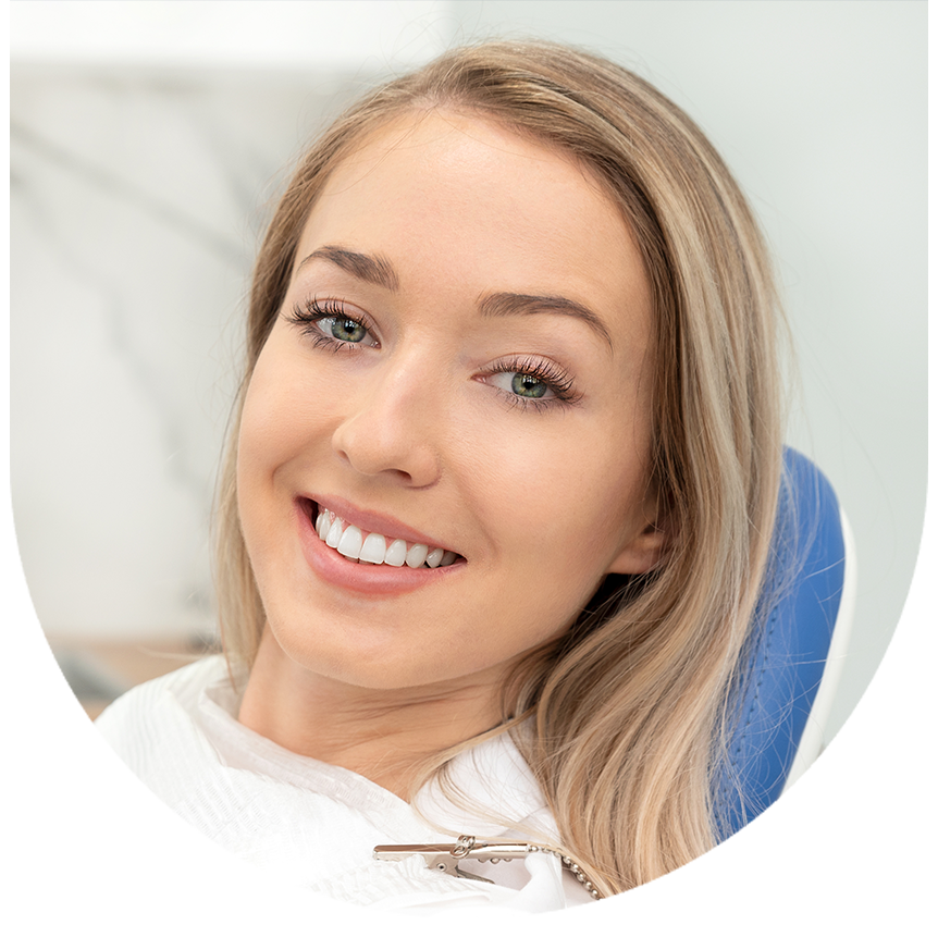 A woman with blonde hair smiling at the camera while sitting in a dental chair.