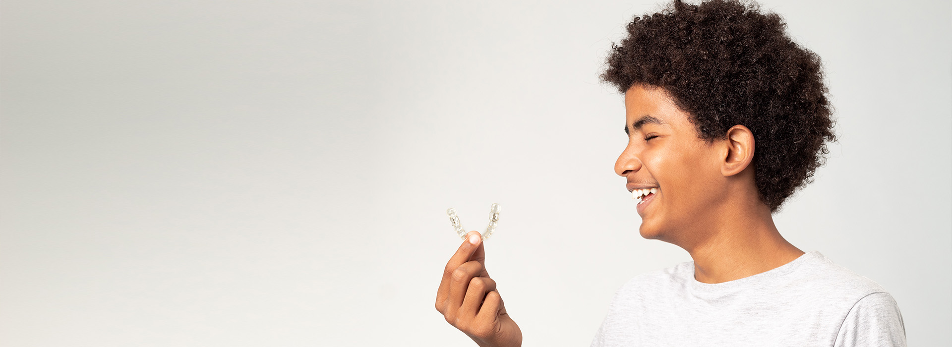 The image shows a person with curly hair holding a small object in their hand against a white background.