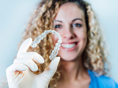 A woman holds up a clear plastic bracelet with a large, round, white bead, smiling at the camera.