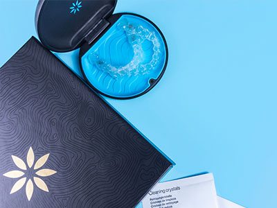 The image shows two open boxes with intricate designs on a table, placed beside a closed box with an embossed design and a blue object inside, against a blue background.