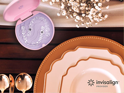 The image shows a table setting with various items including plates, cups, and a cake tin, all arranged on a wooden surface.