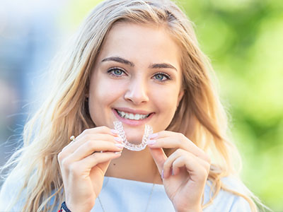 In the image, there s a young woman with a radiant smile, holding up a toothbrush with a toothpaste-covered bristle, possibly promoting oral hygiene.