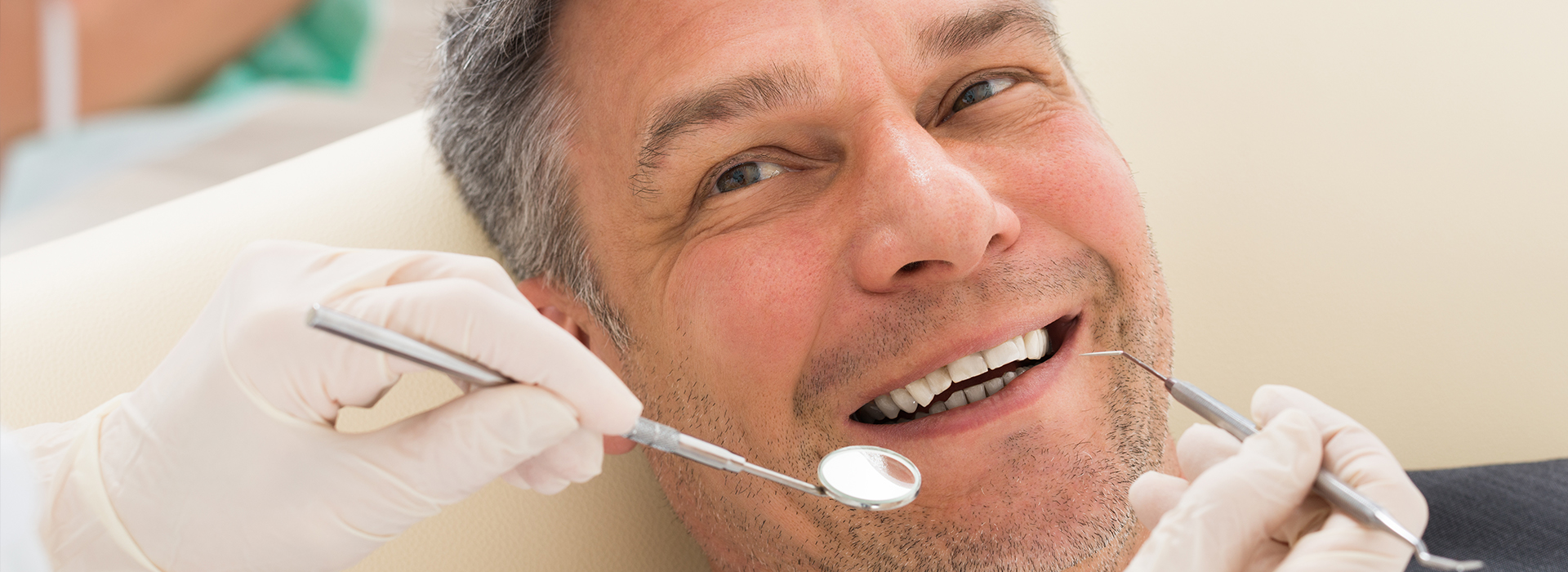 A man sitting in a dental chair with his mouth open, receiving dental treatment from a dentist who is holding a dental tool.