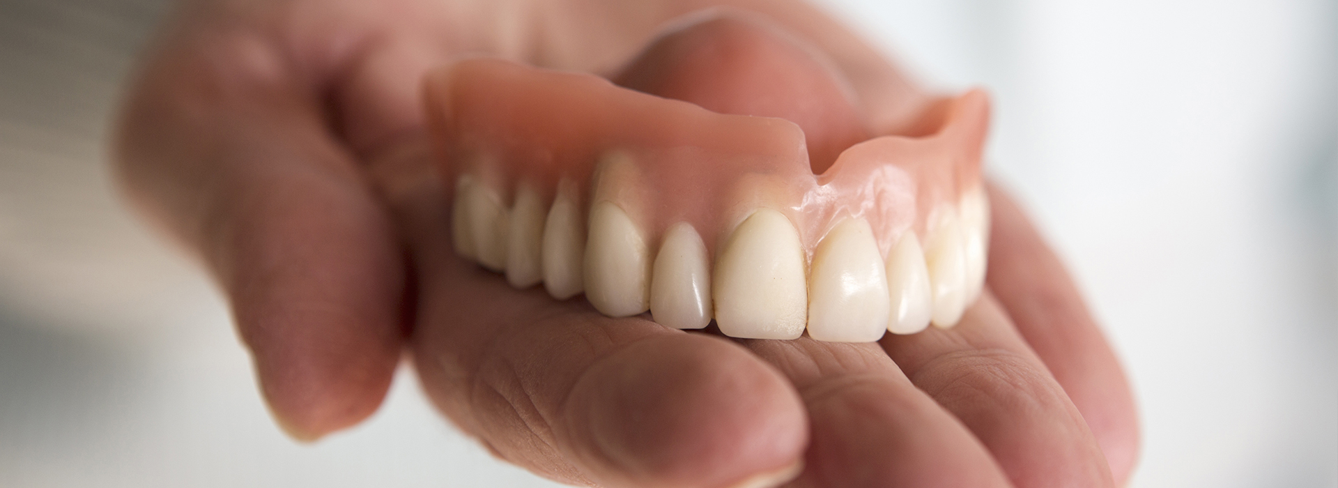 A person s hand holding up a set of dentures with yellowed teeth.