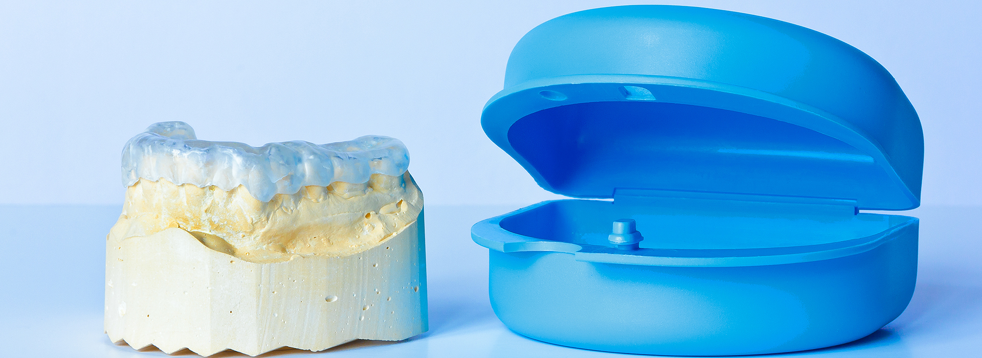 The image displays a pair of blue toothbrushes with yellow bristles next to a single toothpaste tube on a white background.