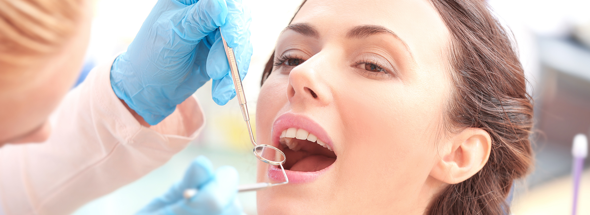 The image shows a woman receiving dental care from a dentist, with a close-up view of her mouth being treated and a person holding a tray of dental instruments.