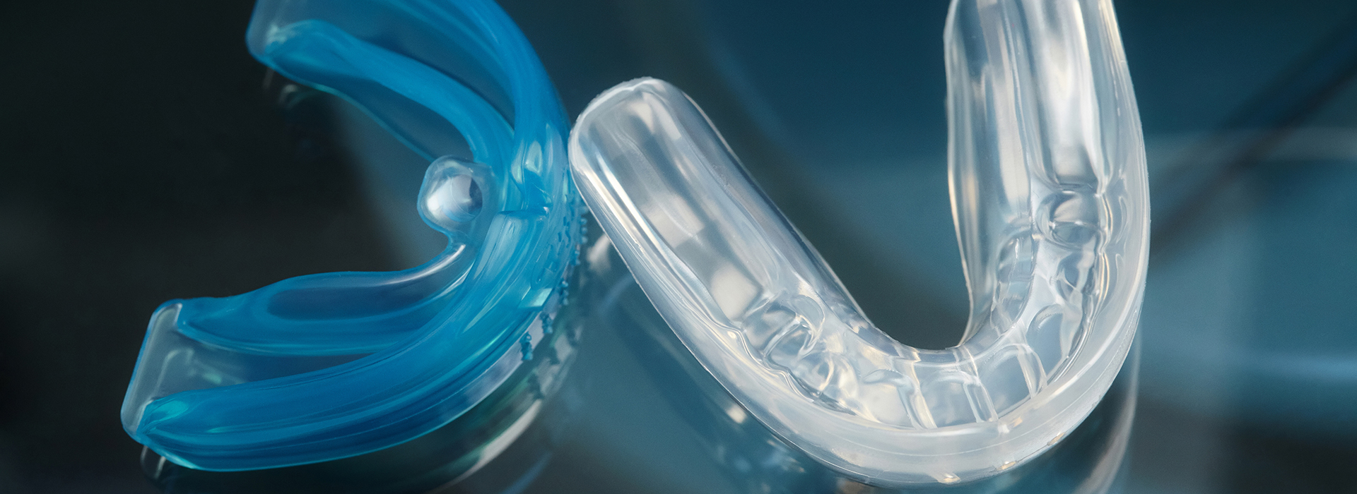 Clear plastic dental braces with blue elastics on a dark background.