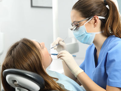 A dental hygienist performing a cleaning procedure on a patient in a dental office setting.