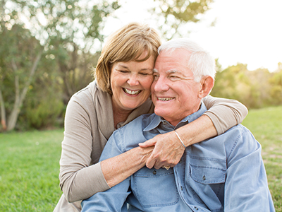 An elderly couple embracing affectionately outdoors during daytime.