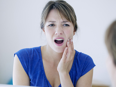 The image shows a woman with her mouth open, possibly expressing surprise or shock, looking into a mirror while another person takes a picture of her from a lower angle.