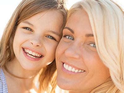 The image shows a woman and a child smiling at the camera, with the adult appearing to be sharing a happy moment with the child.