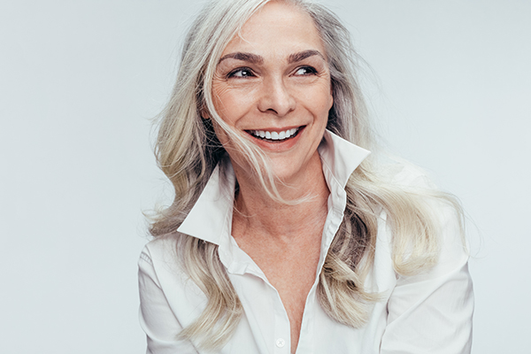 The image shows a woman with short blonde hair wearing a white top, smiling at the camera.