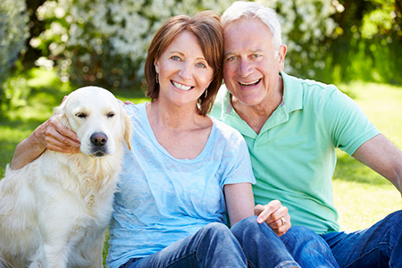 The image shows an elderly couple sitting outdoors with a golden retriever dog between them.