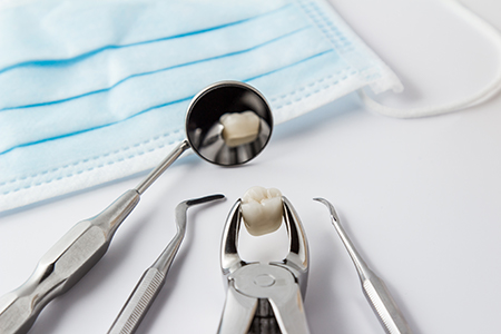 The image shows a collection of dental instruments including a dental mirror, forceps, and other tools, with a focus on a toothbrush being cleaned by a machine, all set against a blue background with a medical mask in the foreground.