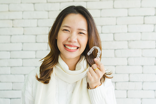 A smiling woman holding a white plastic letter  M  up to her face.