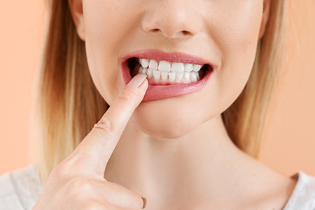 A woman with her finger on her teeth, wearing lipstick, against a pink background.