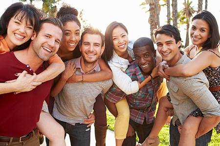 The image features a group of smiling people posing together outdoors, with some members embracing each other and others standing behind them, all appearing happy and relaxed.