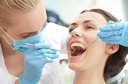 The image depicts a dental hygienist performing a dental procedure on a patient s teeth while wearing protective gloves and equipment, with the patient smiling broadly during the process.