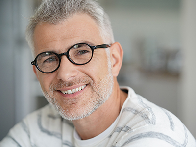 The image shows a man with glasses smiling at the camera from two different angles against a blurred background.