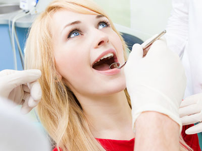 The image shows a woman in a dental chair receiving dental treatment with two dentists assisting her, one performing a procedure while the other holds a camera.
