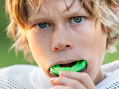 The image shows two photos of a young boy with blonde hair, wearing a football uniform, holding a green object in his mouth.